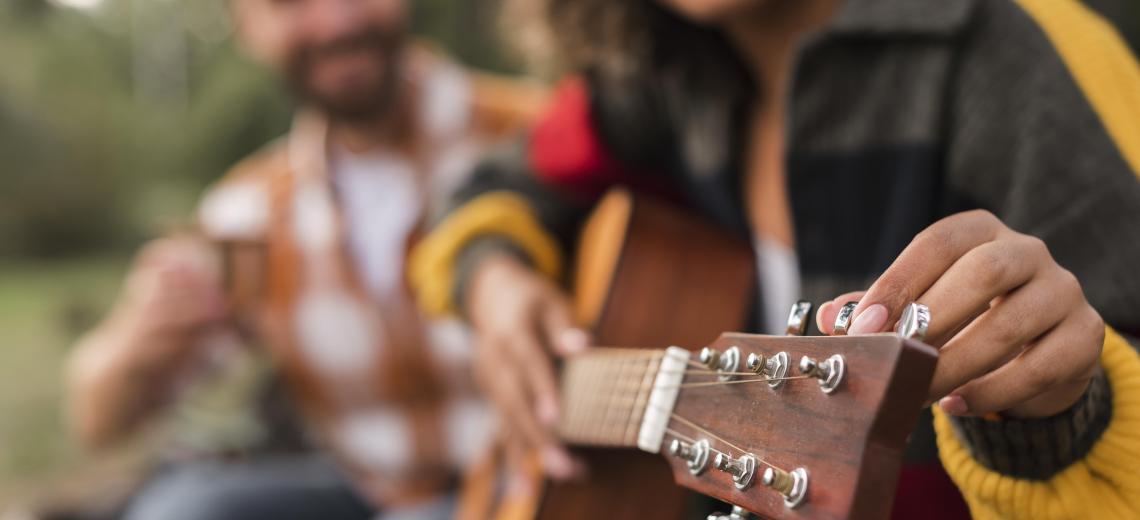 smiley-couple-playing-guitar-outdoors-while-camping © Freepik