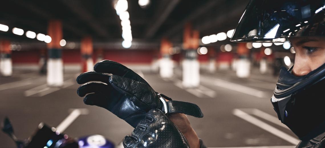 Confident young female racer wearing stylish motorcycle helmet putting on leather gloves, posing isolated in underground parking lot with her blue motorbike. Selective focus on woman's hands © Freepik