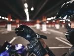 Confident young female racer wearing stylish motorcycle helmet putting on leather gloves, posing isolated in underground parking lot with her blue motorbike. Selective focus on woman's hands © Freepik