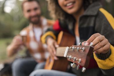 smiley-couple-playing-guitar-outdoors-while-camping